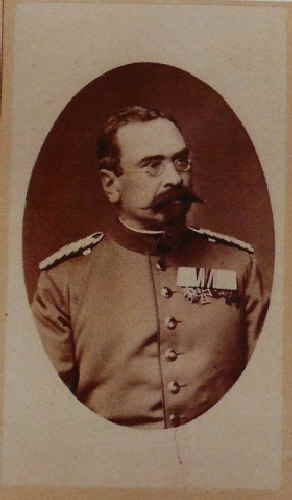 Altes Porträtfoto in Sepia, oval beschnitten: ein Mann mit Brille und breitem Schnurrbart in Uniform mit Schulterstücken und Ordensschnalle, im Halbprofil.