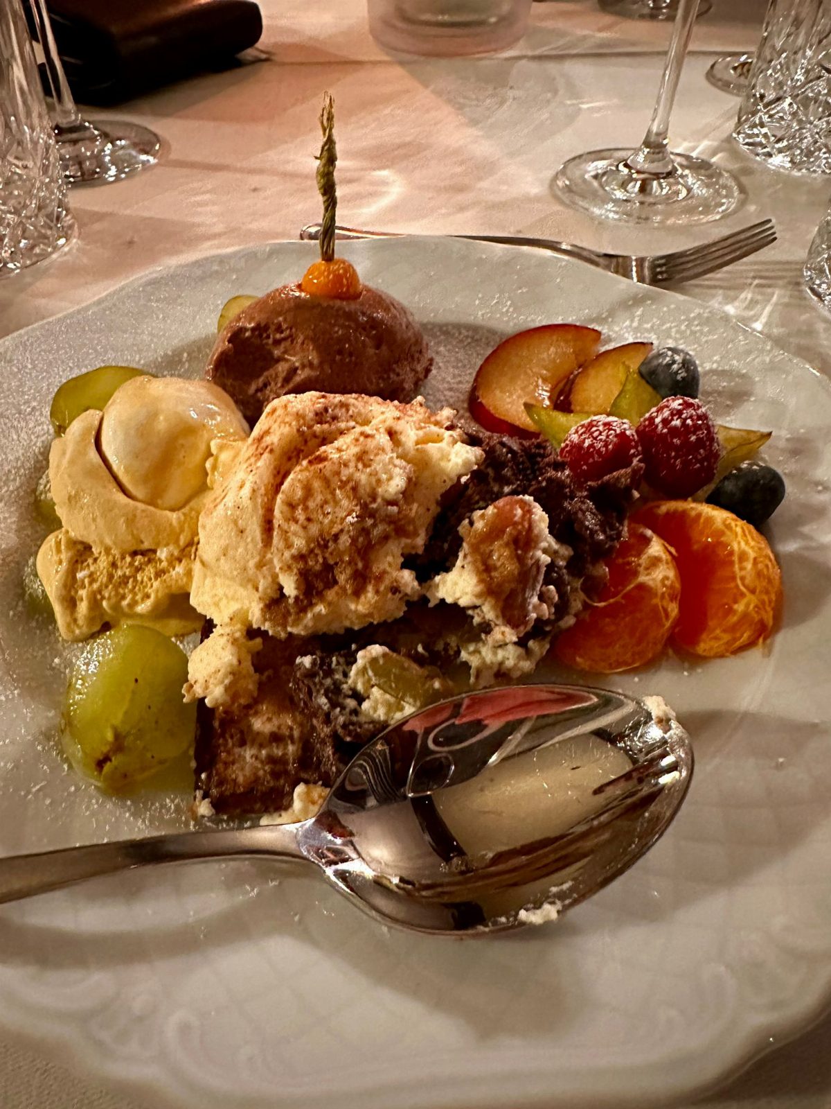 Dessertteller mit einer Nocke Schokoladenmousse, Creme und Gebäck, umlegt mit Weintrauben, Pflaumenspalten, Himbeeren, Heidelbeeren und Mandarinenfilets.